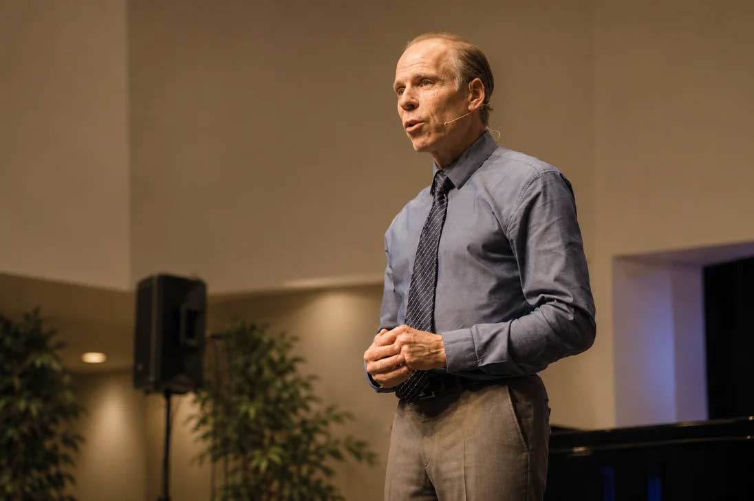 Dr. Joel Fuhrman, wearing a headset microphone, speaking on stage at a live event.
