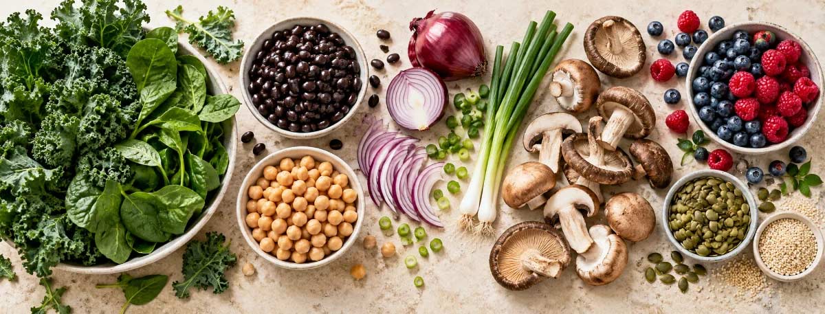 Flat-lay of G-BOMBS foods: leafy greens, beans, onions, mushrooms, berries, and seeds